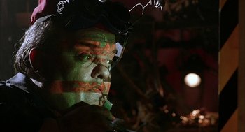 Movie still from “Hardware” (1990), directed by Richard Stanley – A man with a green face painted on his face; Close Up shot, Low angle