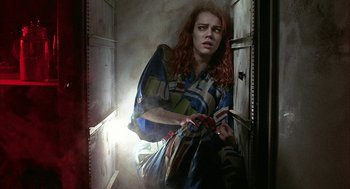 Movie still from “Hardware” (1990), directed by Richard Stanley – A woman with red hair sitting in a doorway; Medium shot, Overhead angle