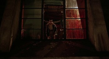 Movie still from “Hardware” (1990), directed by Richard Stanley – A man standing in front of an open window; Wide shot, Low angle