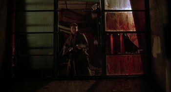 Movie still from “Hardware” (1990), directed by Richard Stanley – A man standing in front of an open window; Wide shot, Low angle