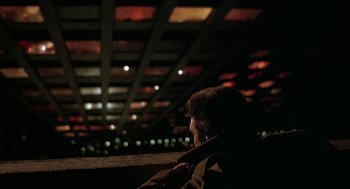 Movie still from “Hardware” (1990), directed by Richard Stanley – A man sitting on a ledge at night; Extreme Wide shot, Low angle