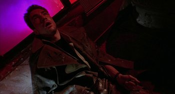 Movie still from “Hardware” (1990), directed by Richard Stanley – A man sitting on the ground in a dark room; Close Up shot, Low angle