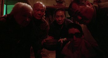 Movie still from “Hardware” (1990), directed by Richard Stanley – A group of people standing in a room with a bowl; Medium shot, High angle