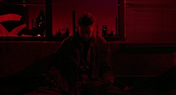 Movie still from “Hardware” (1990), directed by Richard Stanley – A man sitting on a bed in a dark room; Wide shot, Low angle