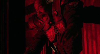 Movie still from “Hardware” (1990), directed by Richard Stanley – A man in a dark room taking a picture with a cell phone; Close Up shot, Low angle