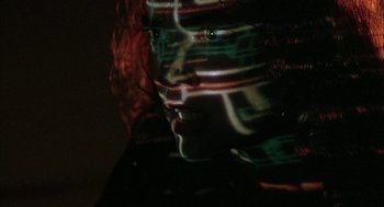 Movie still from “Hardware” (1990), directed by Richard Stanley – A red haired woman with green and red streaks on her face; Extreme Close Up shot, Over the shoulder angle