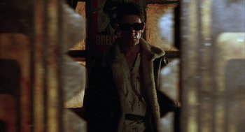 Movie still from “Hardware” (1990), directed by Richard Stanley – A man wearing sunglasses standing in front of a window; Medium shot, Low angle