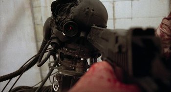 Movie still from “Hardware” (1990), directed by Richard Stanley – A person holding a gun in front of a camera; Extreme Close Up shot, Low angle