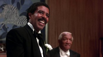 Movie still from “Harlem Nights” (1989), directed by Eddie Murphy – A man in a tuxedo smiles at the camera while a man in a suit stands next to him; Close Up shot, Low angle
