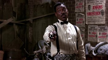 Movie still from “Harlem Nights” (1989), directed by Eddie Murphy – A man in a white shirt and bow tie holding a cell phone; Medium shot, Low angle