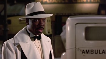 Movie still from “Harlem Nights” (1989), directed by Eddie Murphy – A man wearing a white hat and a white suit; Close Up shot, Over the shoulder angle