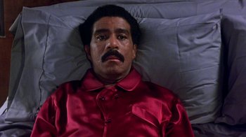 Movie still from “Harlem Nights” (1989), directed by Eddie Murphy – A man laying in a bed wearing a red shirt; Medium shot, Overhead angle