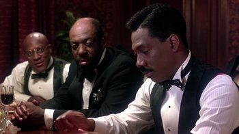 Movie still from “Harlem Nights” (1989), directed by Eddie Murphy – Two men sitting at a table looking at a watch; Medium shot, Over the shoulder angle
