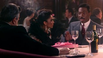 Movie still from “Harlem Nights” (1989), directed by Eddie Murphy – A woman sitting at a dinner table with a man; Medium shot, Over the shoulder angle