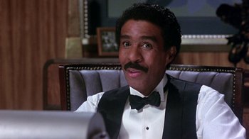 Movie still from “Harlem Nights” (1989), directed by Eddie Murphy – A person sitting in a chair wearing a tuxedo; Close Up shot, High angle