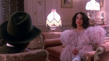Movie still from “Harlem Nights” (1989), directed by Eddie Murphy – A woman sitting on top of a couch in a living room; Medium shot, Over the shoulder angle