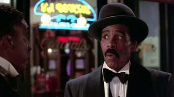 Movie still from “Harlem Nights” (1989), directed by Eddie Murphy – A man wearing a suit and a hat standing in front of a neon sign; Close Up shot, Low angle