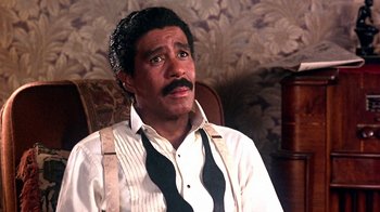 Movie still from “Harlem Nights” (1989), directed by Eddie Murphy – A person sitting in a chair wearing a shirt and tie; Close Up shot, High angle