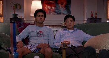 Movie still from “Harold & Kumar Go to White Castle” (2004), directed by Danny Leiner – Two young men sitting on a couch watching television; Medium shot, Low angle