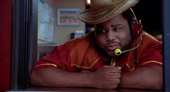 Movie still from “Harold & Kumar Go to White Castle” (2004), directed by Danny Leiner – A man with a straw hat is sitting at a table with a spoon in his mouth; Close Up shot, Low angle