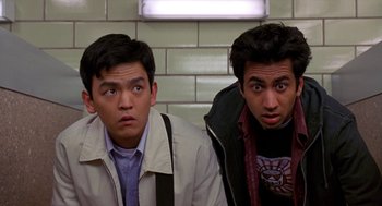 Movie still from “Harold & Kumar Go to White Castle” (2004), directed by Danny Leiner – Two young men sitting next to each other in front of a brick wall; Medium shot, Low angle