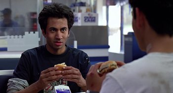Movie still from “Harold & Kumar Go to White Castle” (2004), directed by Danny Leiner – A man sitting at a table with a sandwich in front of him; Close Up shot, Over the shoulder angle